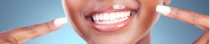 A lady smiling pointing at her white teeth.