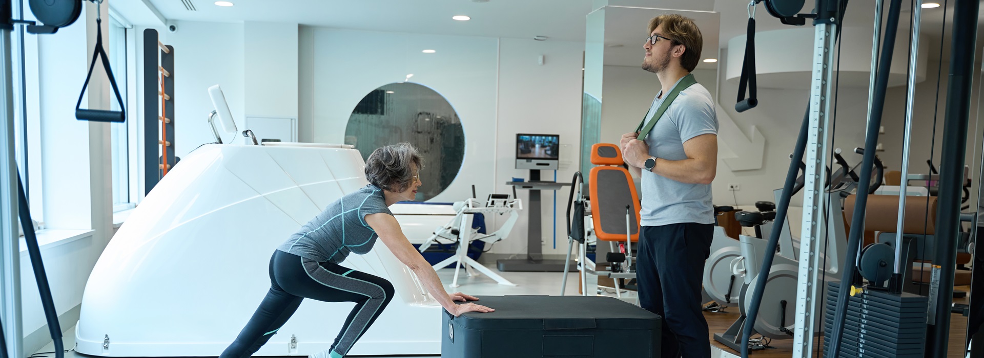 Young man and an elderly woman are in the physio gym