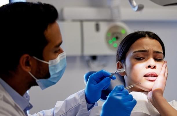 A patient holding her mouth in pain while a dentist examines her.